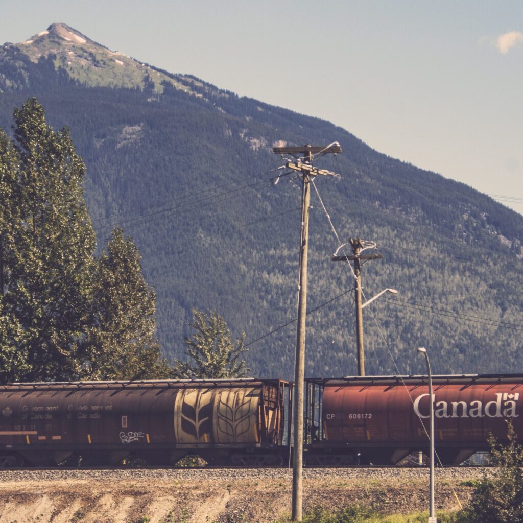 Freight train going through British Columbia. Two grain rail cars are featured, with the word Canada on one.